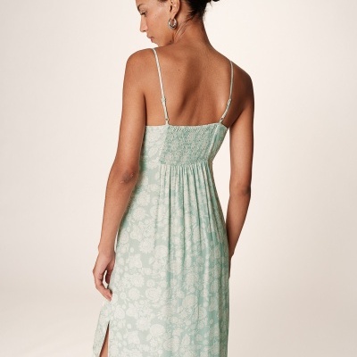 Vestido midi verde claro com padrão floral branco e alças finas, visto de costas, com fenda lateral.
