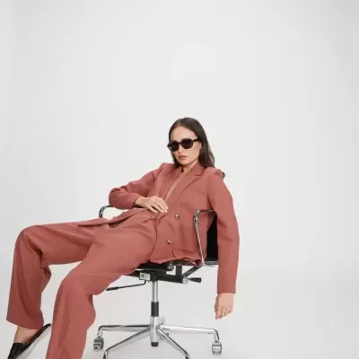 Mulher com fato rosa sentada em cadeira de escritório preta com rodas.