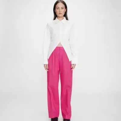 Mulher com camisa branca e calças rosa fúchsia em fundo branco