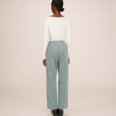 Modelo de costas a usar calças verdes compridas com cintura elástica, blusa branca e sapatos pretos