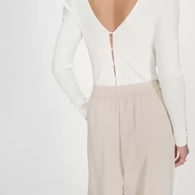 Mulher com camisola branca canelada e calças largas bege vista de costas