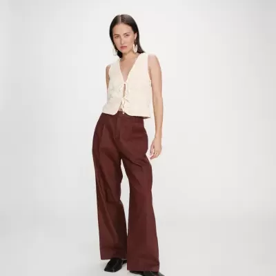 Mulher com blusa branca de crochê e calças largas castanhas em fundo branco.