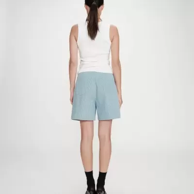Mulher de costas usando calções azuis riscado e top branco com sapatos de salto preto