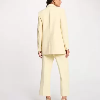 Mulher de costas a usar um blazer e calças amarelas claras com sandálias de salto douradas.
