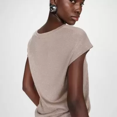 Mulher de costas com t-shirt bege brilhante e brinco metálico