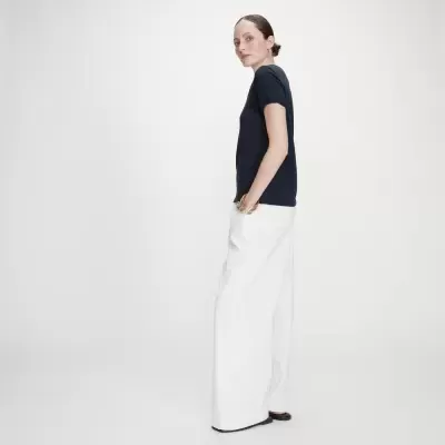 Mulher vestindo t-shirt azul escura e calças largas brancas num fundo branco