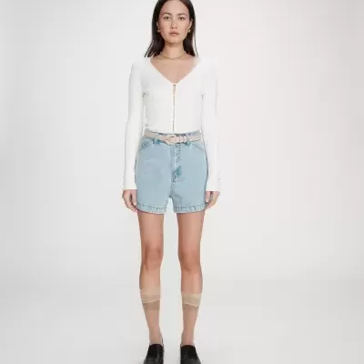 Mulher com camisola branca, calções de ganga, cinto bege, meias transparentes e sapatos pretos