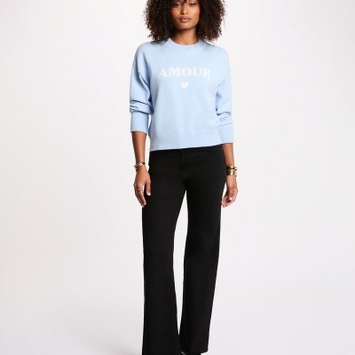 Mulher com camisola azul clara AMOUR e calças pretas num fundo branco.