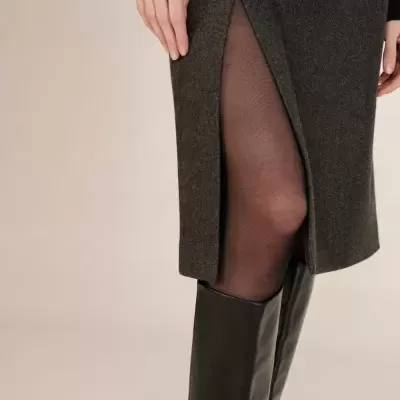 Saia cinzenta com racha lateral, collants pretos e botas pretas até ao joelho.