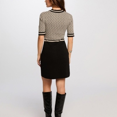 Mulher vista de costas com camisola de padrão geométrico, saia preta curta e botas pretas