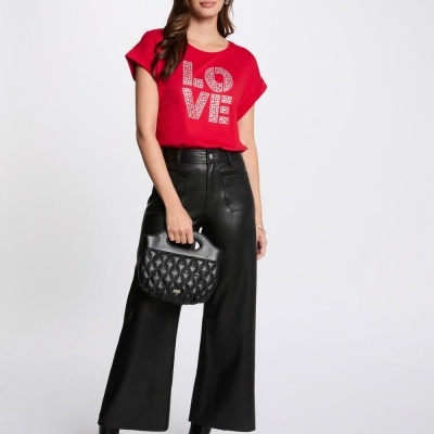 Mulher vestindo tshirt vermelha LOVE, calças pretas largas, botas pretas e segurando mala preta