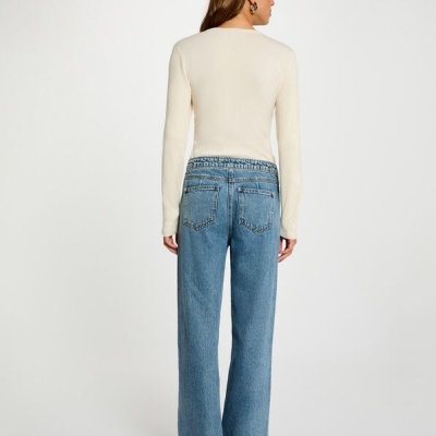 Modelo vista de costas usando calças de ganga azul claro de corte largo e camisola creme de manga comprida