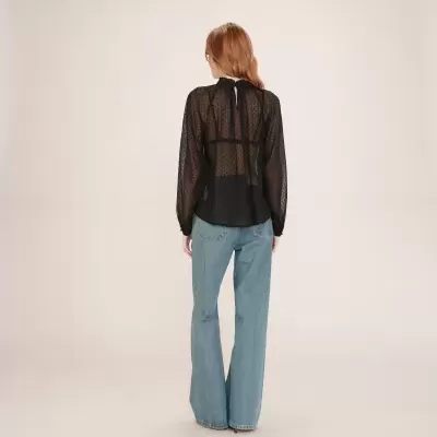 Blusa preta transparente com bolinhas e calças de ganga azuis vistas de costas