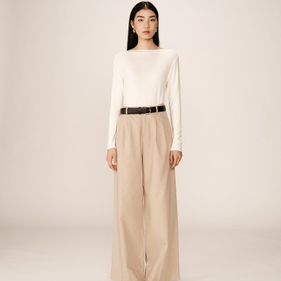 Mulher vestindo camisola branca, calças largas bege, cinto preto e sapatos pretos