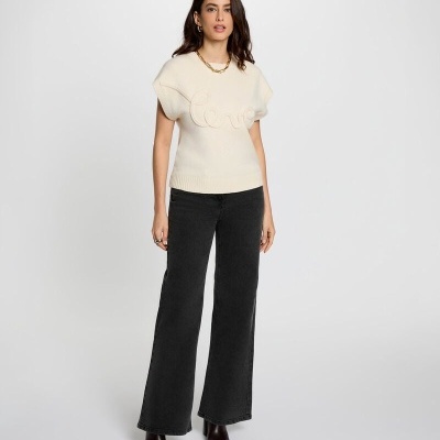 Mulher em fundo branco com camisola branca com palavra Love, calças pretas largas e botas castanhas