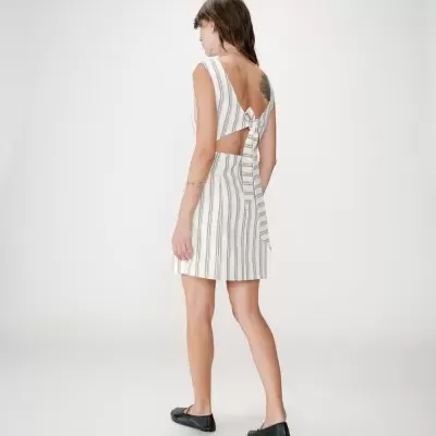 Vestido curto às riscas com costas abertas e laço, calçado preto, fundo branco.