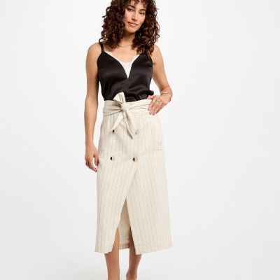 Mulher com saia midi bege com riscas e top preto em fundo branco