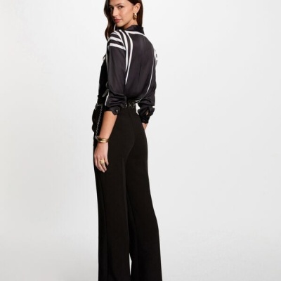 Mulher com camisa preta de padrões brancos e calças pretas largas