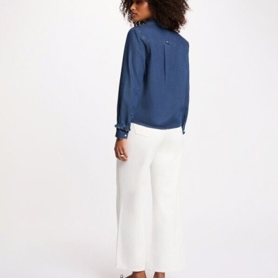 Mulher de costas com camisa azul, calças brancas largas e sapatilhas pretas.