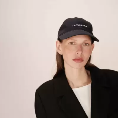 Boné preto GRACE&MILA com mulher vestindo casaco preto e t-shirt branca em fundo neutro