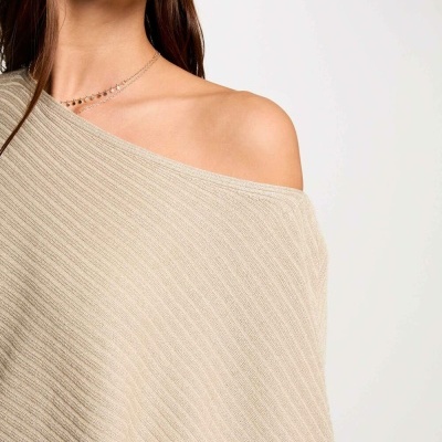 Camisola bege de malha com ombro descoberto e colar delicado num fundo branco.