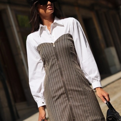 Mulher a usar vestido branco com corpo cinzento riscado e boina preta numa rua urbana