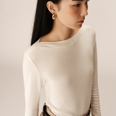 Mulher com camisa branca de manga comprida, calças bege e cinto preto