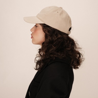 Mulher de perfil com boné bege e casaco preto