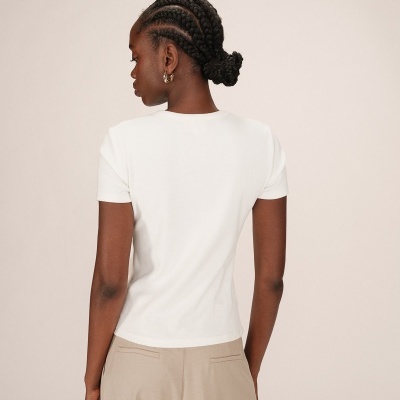 Mulher de costas com t-shirt branca e calças bege num fundo neutro