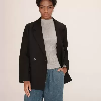 Mulher a usar casaco preto, camisola cinza canelada e jeans azuis largos