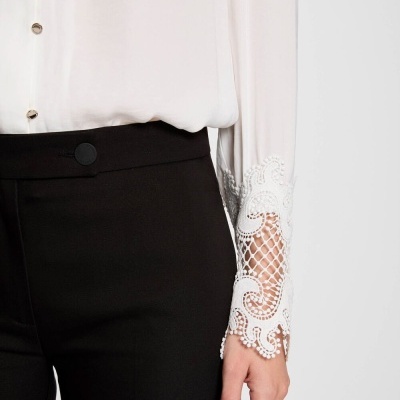 Camisa branca com punho em renda e calças pretas com botão na cintura.