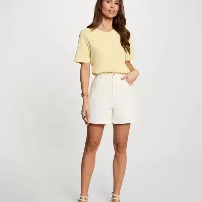 Mulher com t-shirt amarela clara, calções brancos e sandálias brancas com tachas
