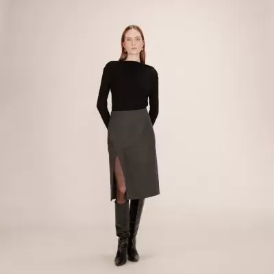 Mulher com blusa preta, saia cinzenta com racha frontal e botas pretas