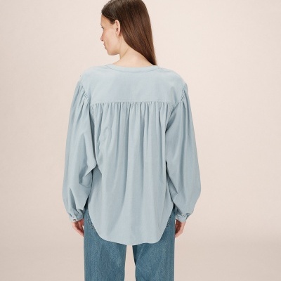 Blusa azul clara de manga comprida larga com pregas nas costas e calças de ganga azuis