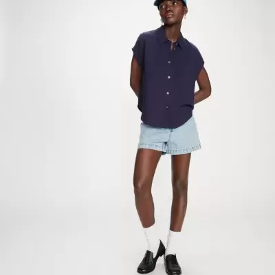 Modelo com camisa azul escura, calções jeans claros, meias brancas, sapatos pretos e boné azul claro