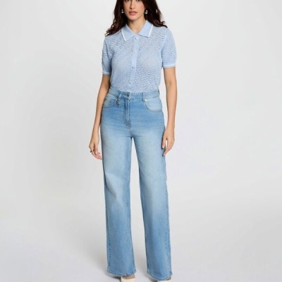 Mulher de pé com camisola de malha azul clara, calças de ganga largas e sapatos brancos