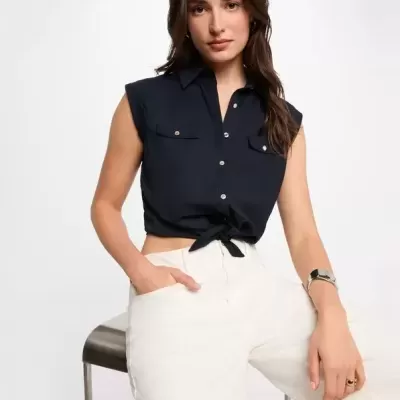 Top feminino azul escuro sem mangas com botões e bolso, calças brancas, mulher sentada