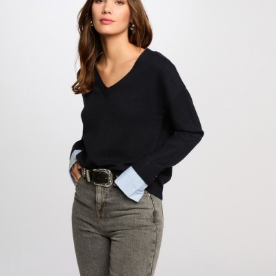 Mulher com camisola preta, camisa azul e jeans cinza claro