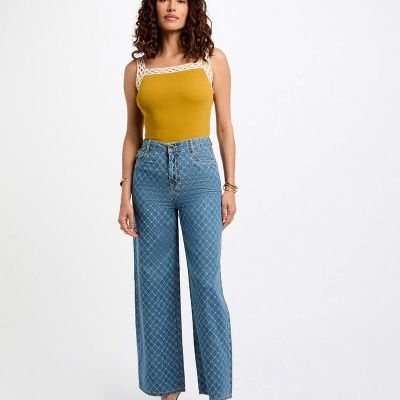 Mulher vestindo top amarelo com alças de crochê e calças de ganga azuis com padrão de linhas brancas.