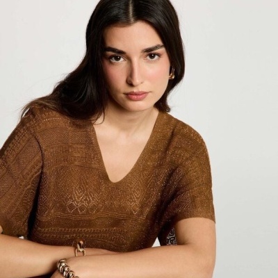 Mulher com blusa castanha de tricô e acessórios dourados sentada