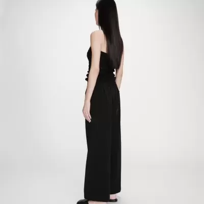 Mulher de costas com top preto sem alças e calças largas pretas