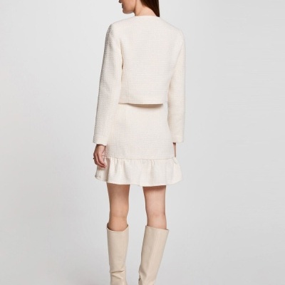 Mulher de costas com casaco e saia creme de tecido texturizado e botas creme