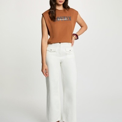 Mulher com blusa castanha sem mangas, calças brancas largas e botas castanhas de salto alto