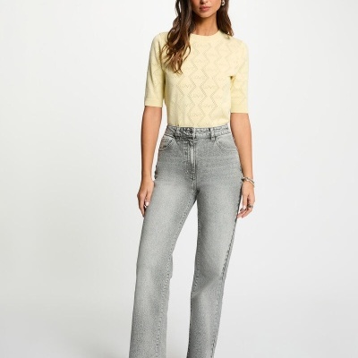 Mulher com camisola amarela e calças de ganga cinza em fundo branco