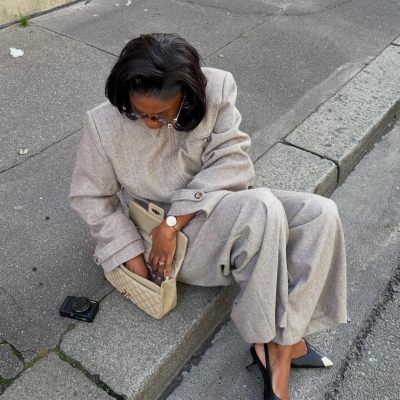 Mulher sentada na berma de estrada com fato cinzento e sapatos pretos de salto baixo