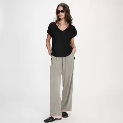 Mulher com t-shirt preta de malha e calças largas bege com chinelos pretos.