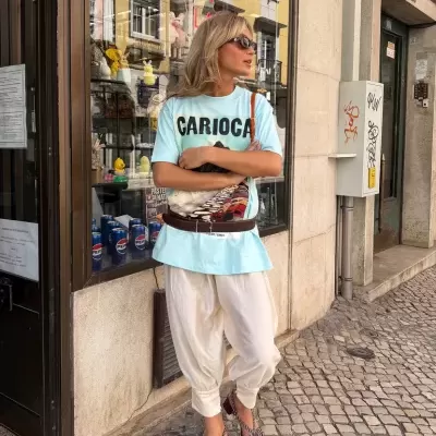 Pessoa com roupa casual e acessórios junto a montra em calçada de pedra