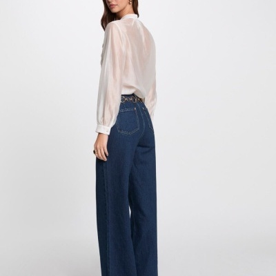 Calças de ganga azul escuro largas com cinto dourado e camisa branca manga comprida.