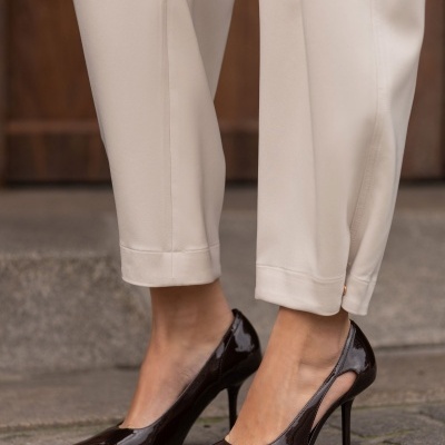 Sapatos de salto alto castanhos em verniz com calças bege claras e pavimento de pedra