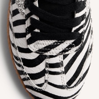 Sapatilha com padrão de riscas zebrado em preto e branco com atacadores pretos e detalhe prateado